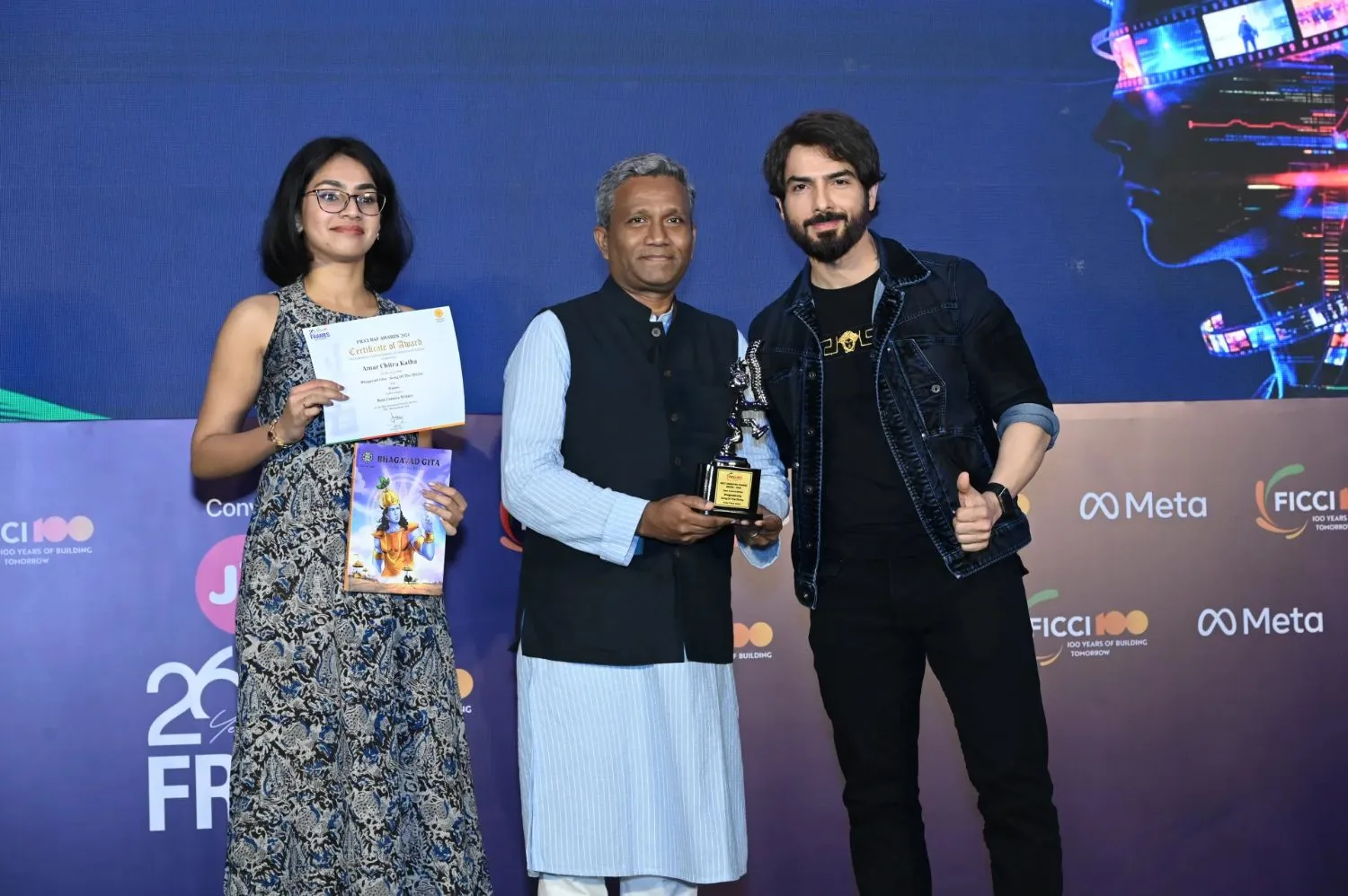 Savio Mascarenhas holds the Best Comics Writer trophy for Amar Chitra Katha on stage, with the certificate and book held beside him.