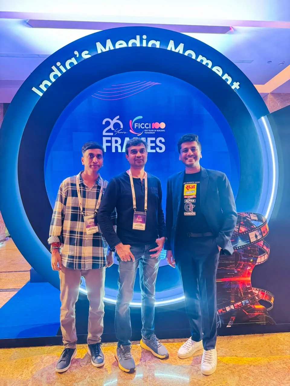Three Indian Comics Association representatives standing in front of the FICCI FRAMES arch in Mumbai.